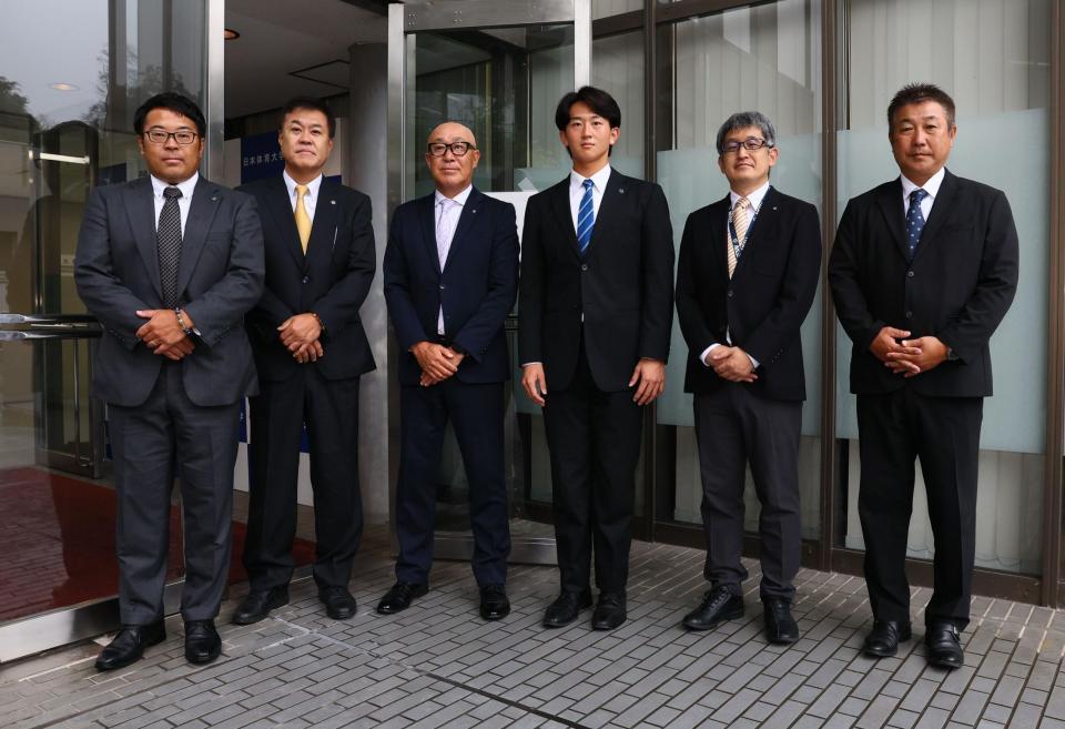 指名あいさつで記念撮影に応じる東編成ディレクター、平塚スカウト、畑山統括スカウト、日体大・馬場拓海、ドラフト２位指名の日体大・大石部長、日体大・古城監督（撮影・中島達哉）