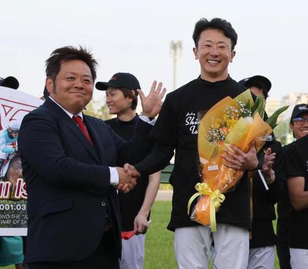 マイネルグロンを管理した青木調教師から花束を贈られ握手する石神深一
