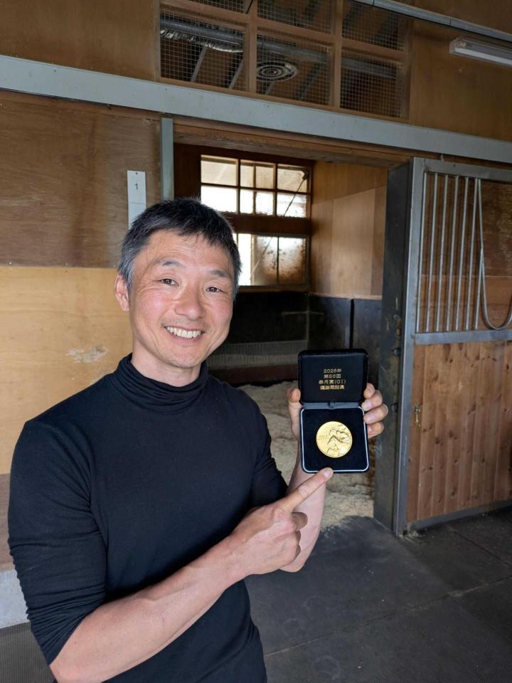 　皐月賞の金メダルを手に笑顔を見せる房野陽介助手